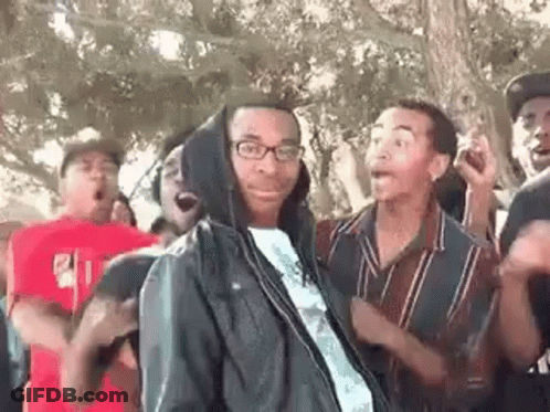 A Group Of Young Men Are Dancing In A Park . One Of The Men Is Wearing Glasses And A Hooded Jacket . GIF
