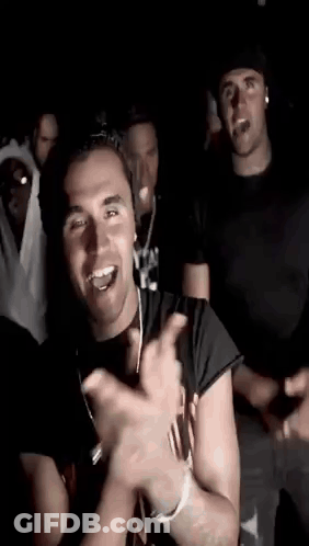 A Group Of Young Men Are Dancing Together In A Dark Room And Smiling . GIF
