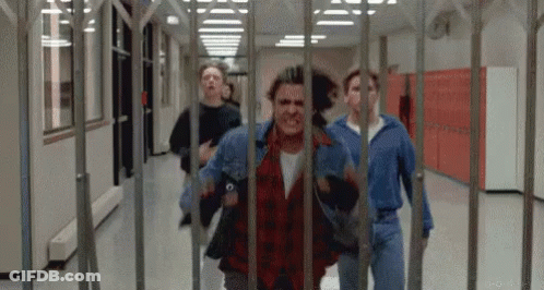 A Group Of Young Men Are Running Through A Hallway Behind A Fence . GIF