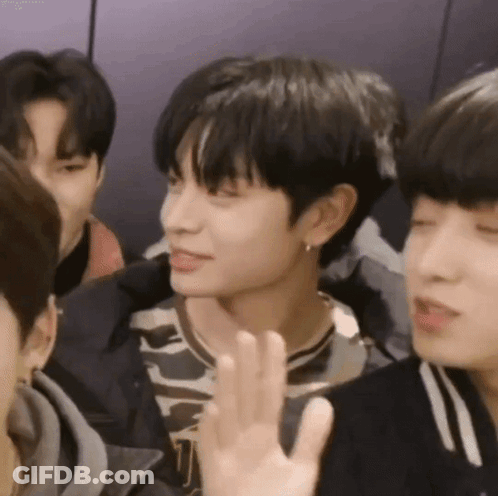 A Group Of Young Men Are Sitting Around A Table And One Of Them Is Waving His Hand . GIF