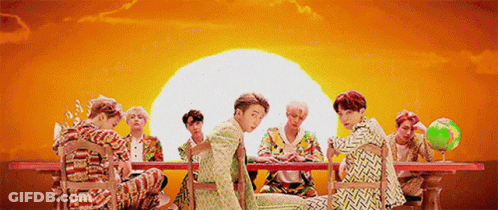 A Group Of Young Men Are Sitting Around A Table With A Globe In Front Of A Sunset . GIF