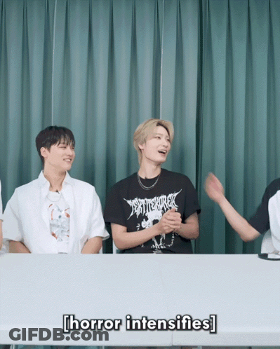 A Group Of Young Men Are Sitting At A Table And One Of Them Is Wearing A Black Shirt That Says " Horror Intensifies " GIF