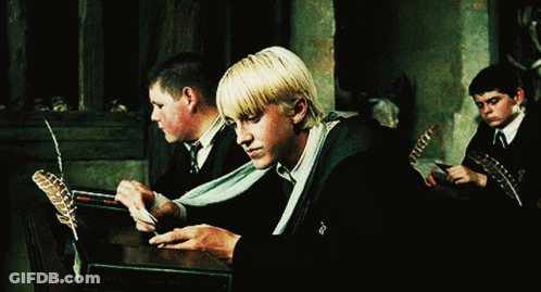 A Group Of Young Men Are Sitting At A Table With Feathers And A Book That Says Harry Potter On It GIF