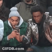A Group Of Young Men Are Sitting In A Crowd Looking At Their Cell Phones . GIF