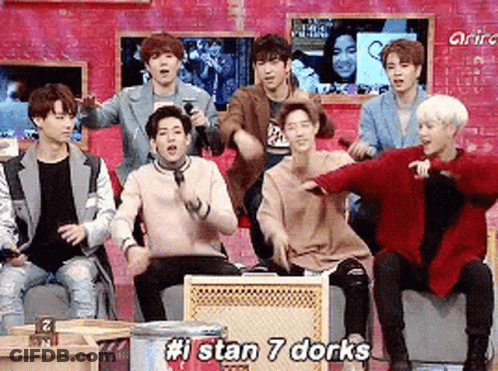 A Group Of Young Men Are Sitting In Front Of A Brick Wall And Dancing Together . GIF
