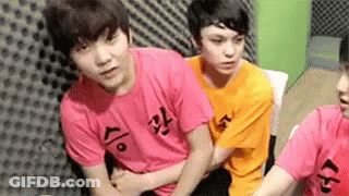 A Group Of Young Men Are Sitting Next To Each Other In A Room Wearing Pink And Orange Shirts . GIF
