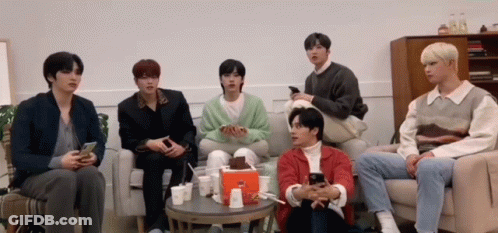 A Group Of Young Men Are Sitting On A Couch Looking At Their Cell Phones . GIF