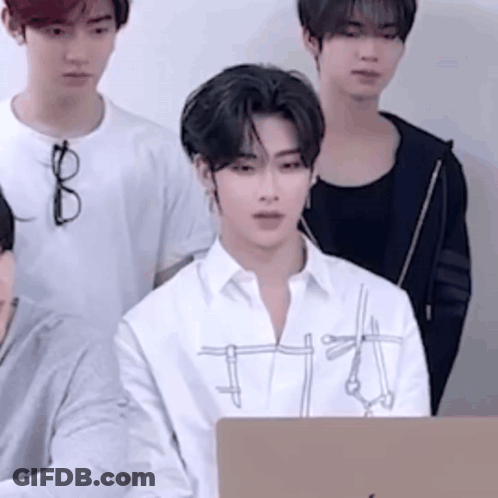 A Group Of Young Men Are Standing Around A Laptop Computer . One Of The Men Is Wearing Glasses . GIF