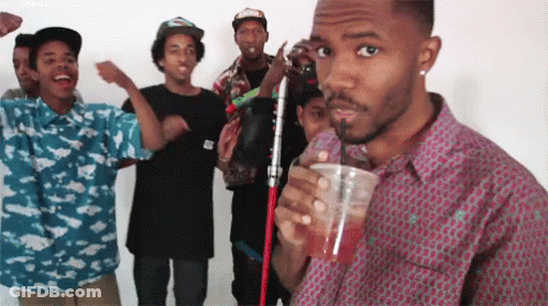 A Group Of Young Men Are Standing Around A Man Drinking A Drink Through A Straw GIF