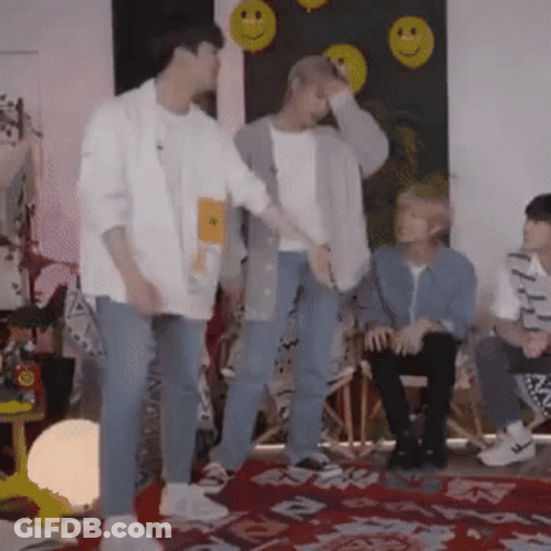 A Group Of Young Men Are Standing In A Room With Smiley Faces On A Wall . GIF