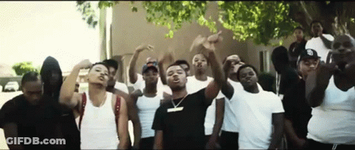 A Group Of Young Men Are Standing In Front Of A Building With Their Hands In The Air . GIF