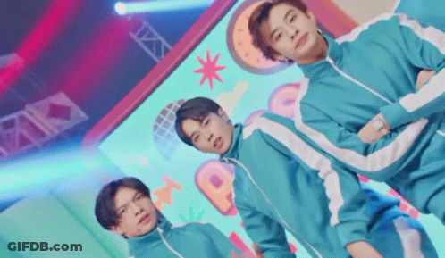 A Group Of Young Men Are Standing Next To Each Other On A Stage In Squid Game Costumes . GIF