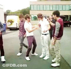 A Group Of Young Men Are Standing On A Sidewalk Talking To Each Other GIF