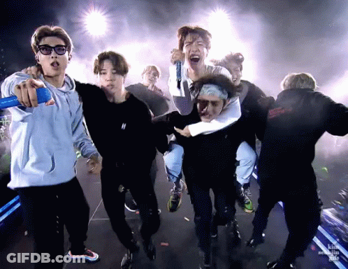 A Group Of Young Men Are Standing On A Stage Holding Microphones And Singing Into Them . GIF