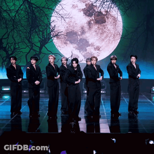 A Group Of Young Men Are Standing On A Stage In Front Of A Full Moon GIF