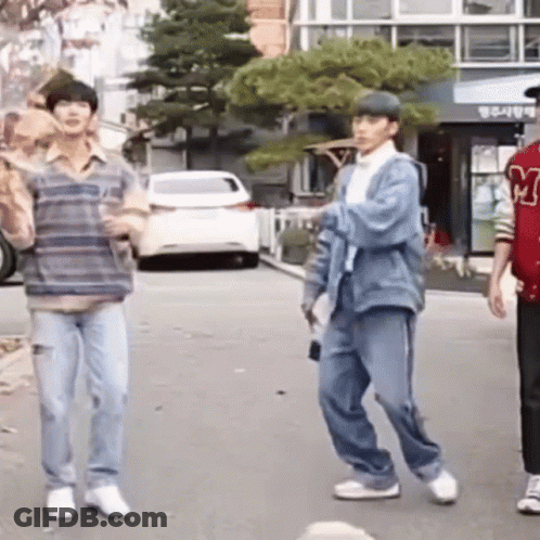 A Group Of Young Men Are Standing On A Street . GIF