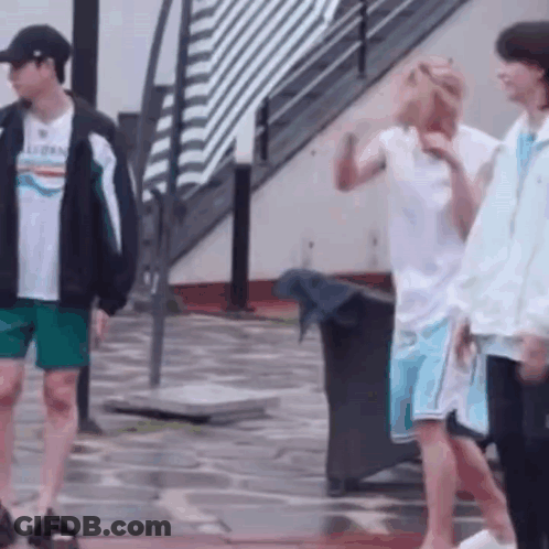 A Group Of Young Men Are Standing On A Wet Sidewalk . GIF