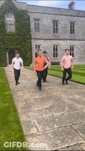 A Group Of Young Men Are Walking Down A Stone Walkway In Front Of A Large Building GIF