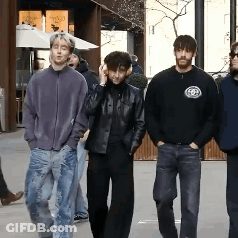A Group Of Young Men Are Walking Down A Street And One Of Them Is Wearing Headphones GIF