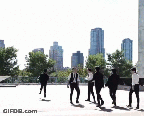 A Group Of Young Men Are Walking In Front Of A City Skyline GIF