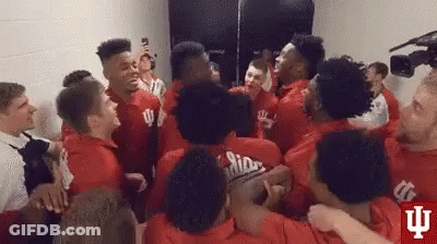 A Group Of Young Men In Red Shirts Are Hugging Each Other In A Room . GIF