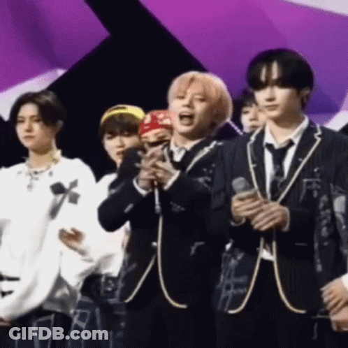 A Group Of Young Men In Suits And Ties Are Standing On A Stage Holding Microphones . GIF