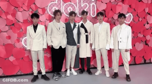 A Group Of Young Men In Suits Are Standing In Front Of A Wall Made Of Hearts . GIF