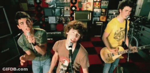 A Group Of Young Men Singing And Playing Guitars In Front Of A Wall That Says Try On It GIF