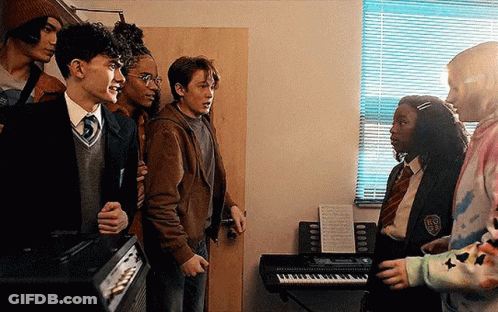 A Group Of Young People Are Standing Next To Each Other In A Room With A Piano . GIF