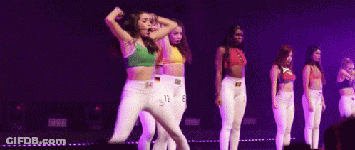 A Group Of Young Women Are Dancing On A Stage With Purple Lights . GIF