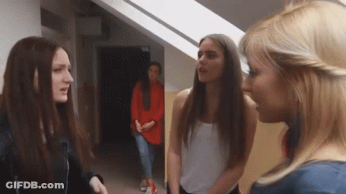 A Group Of Young Women Are Standing In A Hallway Talking To Each Other . GIF