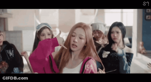 A Group Of Young Women Are Standing In A Room And One Of Them Is Holding A Pink Hoodie GIF
