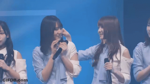 A Group Of Young Women Are Standing In Front Of A Blue Background And One Of Them Is Holding A Microphone GIF
