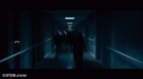 A Group Of Zombies Are Walking Down A Hallway . GIF