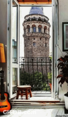 A Guitar Sits On The Floor In Front Of A Balcony With A View Of A Tower GIF