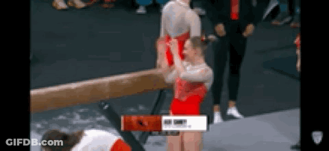 A Gymnast Is Doing A Trick On A Balance Beam While Another Gymnast Looks On . GIF
