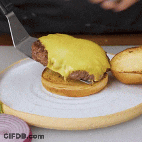 A Hamburger Is Being Served On A White Plate With A Spatula GIF