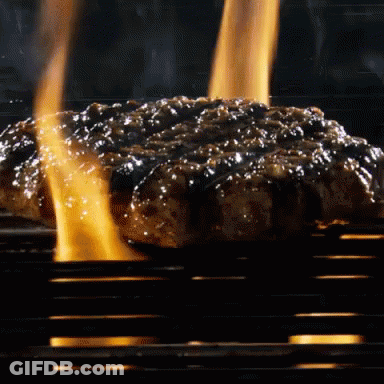 A Hamburger Is Cooking On A Grill With Flames Behind It GIF