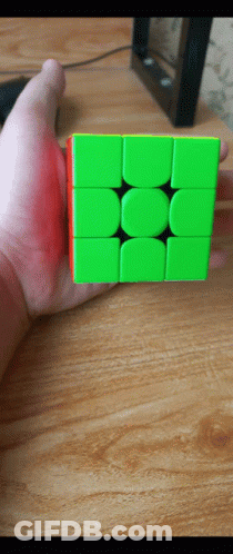 A Hand Is Holding A Green And Red Cube On A Wooden Table GIF