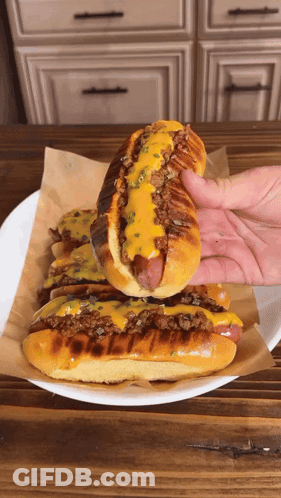 A Hand Is Holding A Hot Dog On A Plate GIF