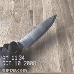 A Hand Is Holding A Knife On A Wooden Surface . GIF