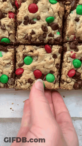 A Hand Is Reaching For A Cookie Bar With M & M 'S GIF