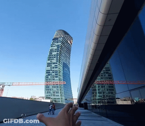A Hand Reaches Up Towards A Tall Building With A Blue Sky In The Background GIF