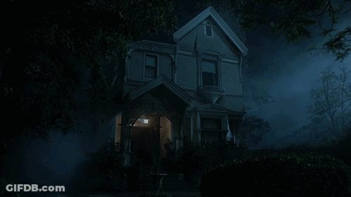 A Haunted House Is Lit Up At Night With Trees In The Foreground GIF