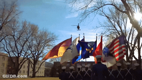 A Helicopter Flies Over A Line Of Soldiers Holding Flags Including One That Says ' Army ' On It GIF