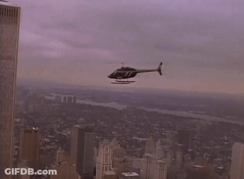 A Helicopter Is Flying Over A City With A Few Buildings In The Background GIF