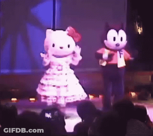 A Hello Kitty Mascot And Felix The Cat Mascot Are Dancing On A Stage In Front Of A Crowd . GIF