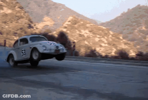 A Herbie The Beetle Is Driving Down A Road With Mountains In The Background GIF