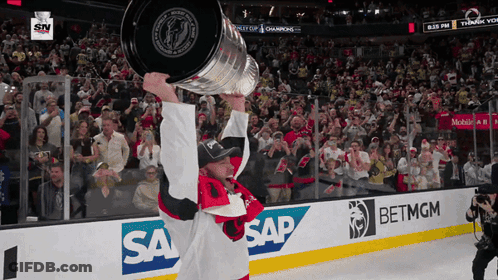A Hockey Player Holds Up A Trophy In Front Of A Crowd With Sap And Betmgm Advertisements GIF