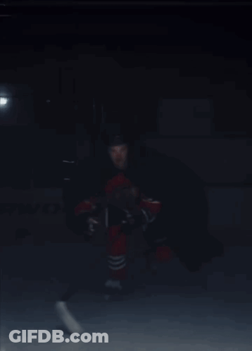 A Hockey Player In A Red And Black Uniform Is Holding A Hockey Stick GIF